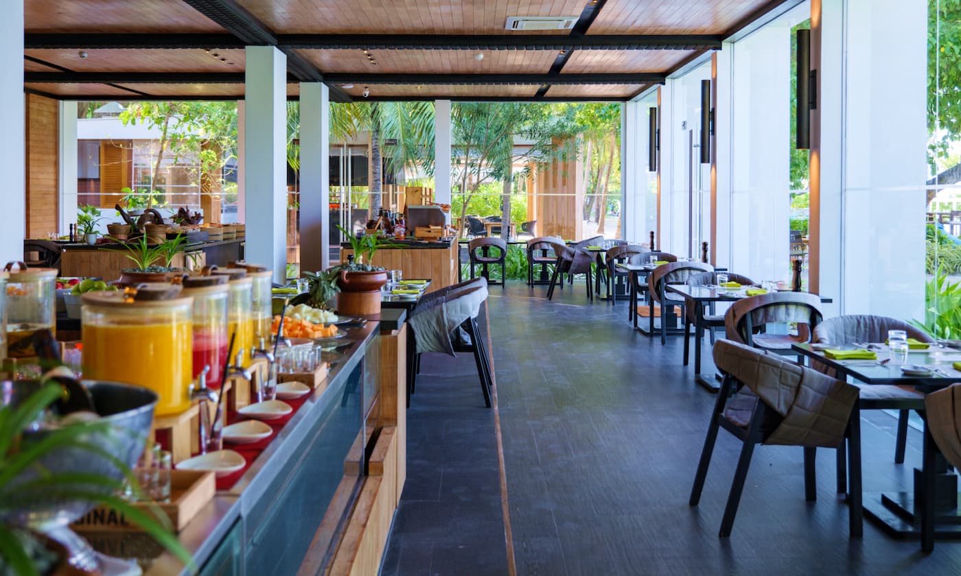 A restaurant with the food cabinet to the left, There are tables and chaors in rows in frotn with space to walk in between