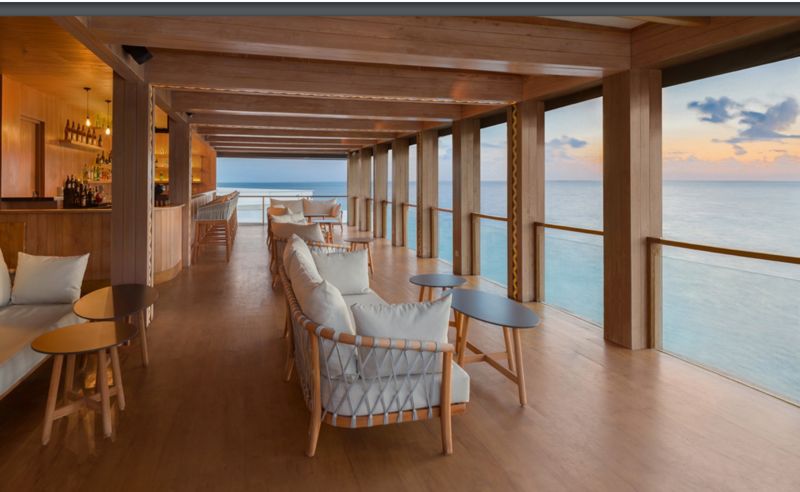 long wooden room with wooden beams above. There are chairs facing out to the sea. The room is on stilts over the sea