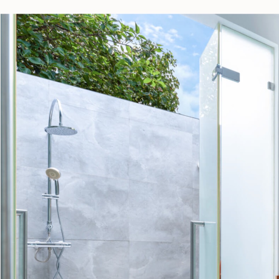 View through a doorway to an outdoor roll in shower. The shower has a hand held shower as well as an overhead one