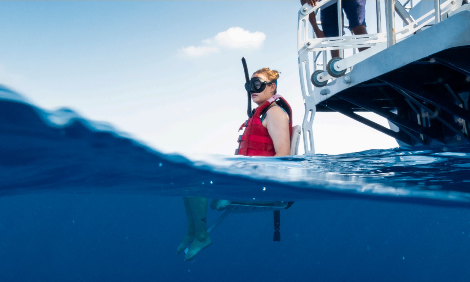 A woman being lowered into the sea from a boat with a hoist.  She is wearing a red costume and a snorkelling mask